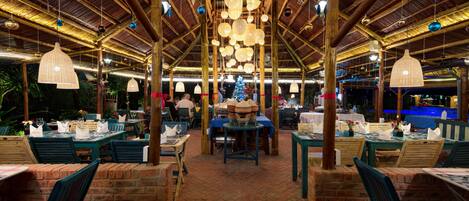 An outdoor restaurant with brick walls, wooden tables, and hanging light fixtures.