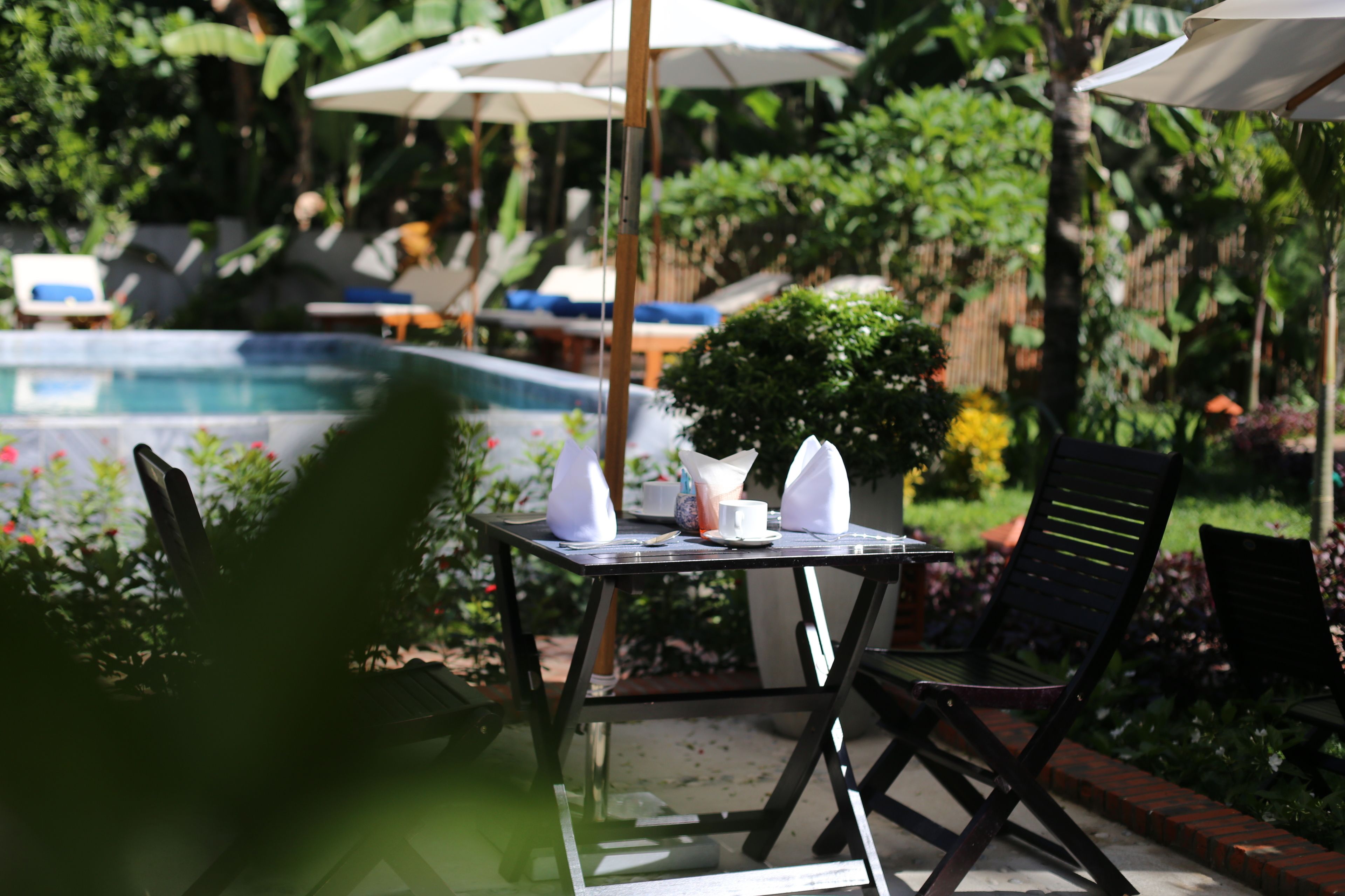 A glass-enclosed outdoor seating area with a table, chairs, and umbrellas, overlooking a swimming pool.