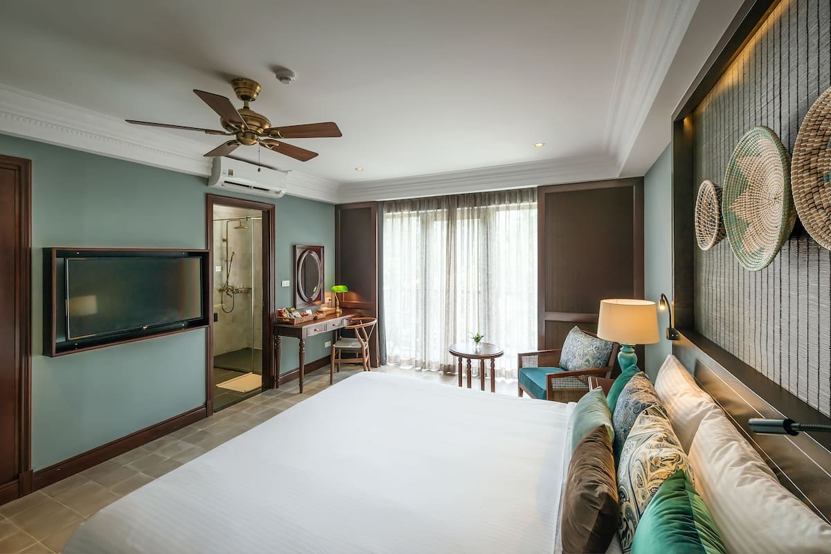 A hotel room with a large bed, a desk with a chair, a television, and a ceiling fan.