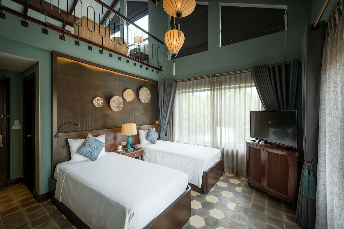 A hotel room with two beds, a TV, and a balcony with a wooden railing.