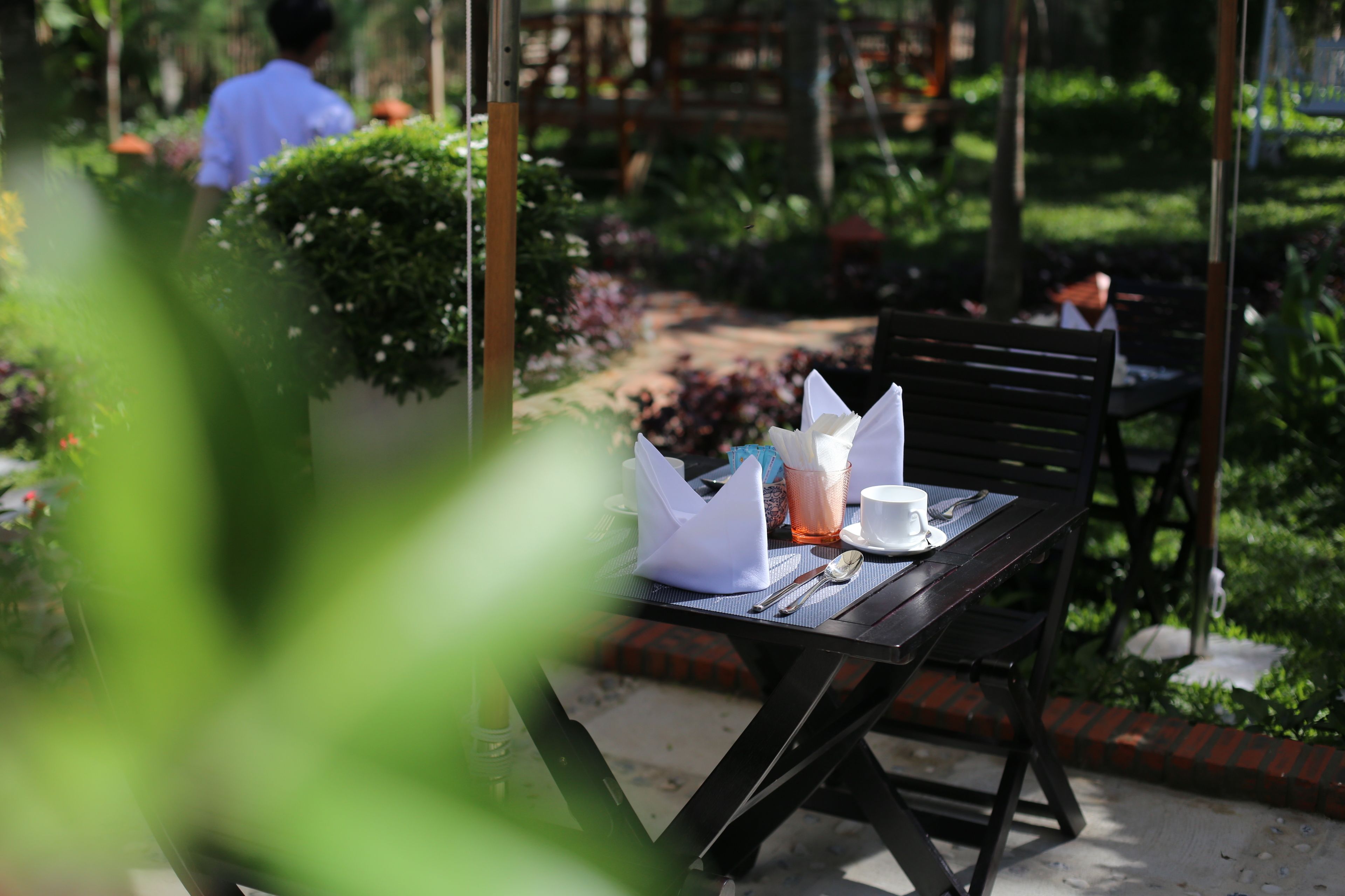 An outdoor dining area with a table set for two, surrounded by greenery.