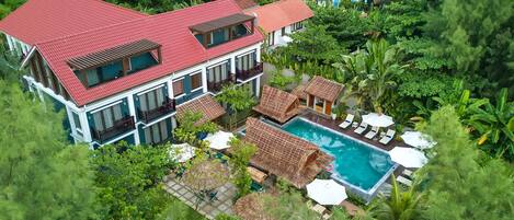 An aerial view of a resort with multiple buildings, a swimming pool, and lush greenery.
