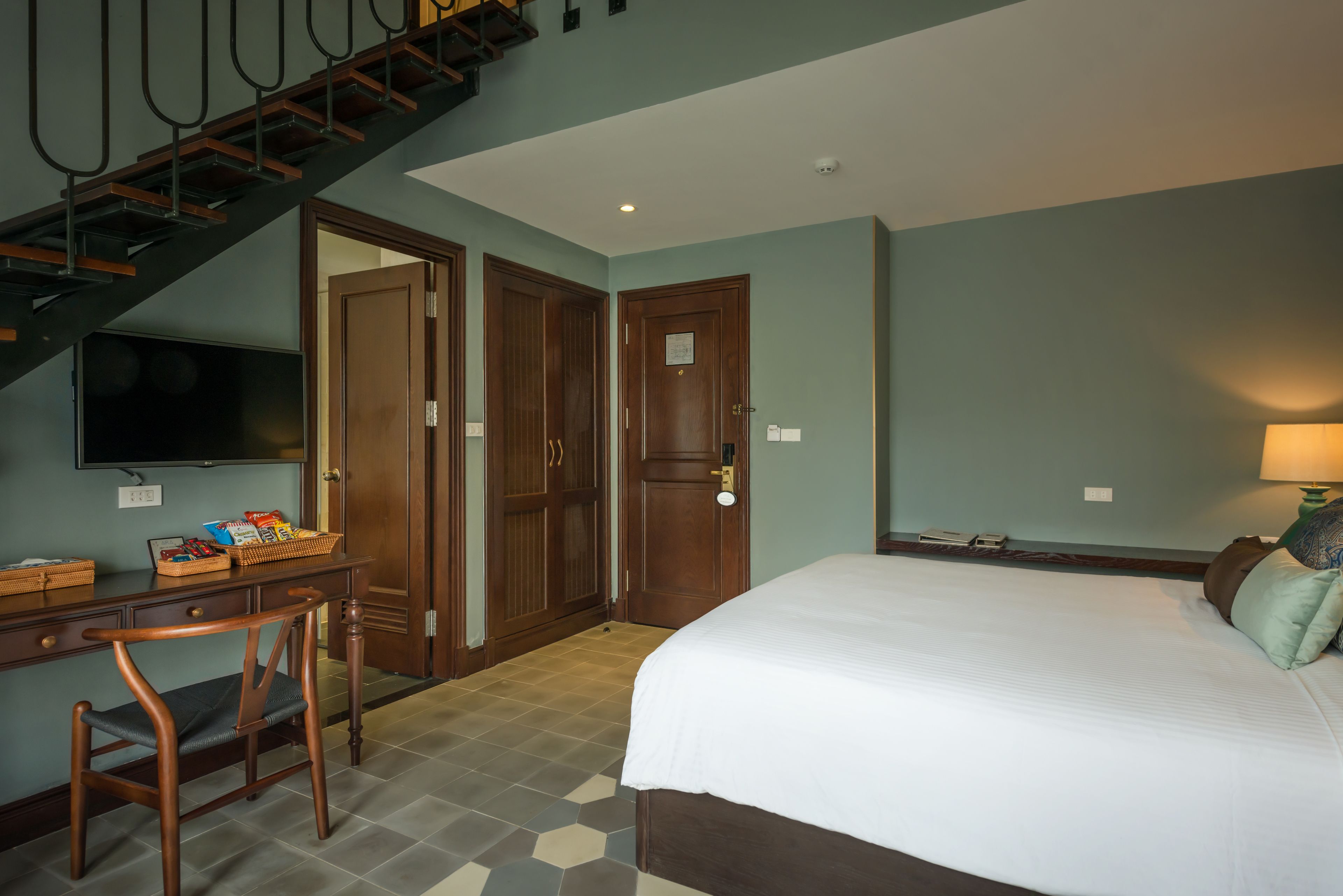 A hotel room with a bed, desk, chair, and a staircase.