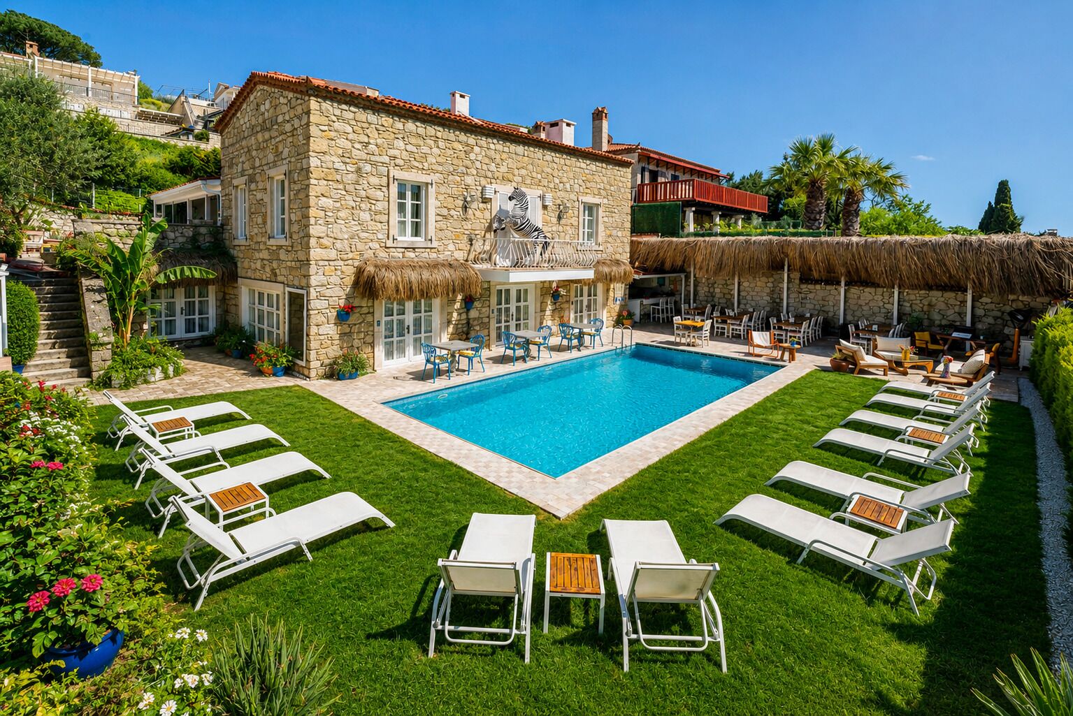 A stone building with a swimming pool, lounge chairs, and a thatched roof.
