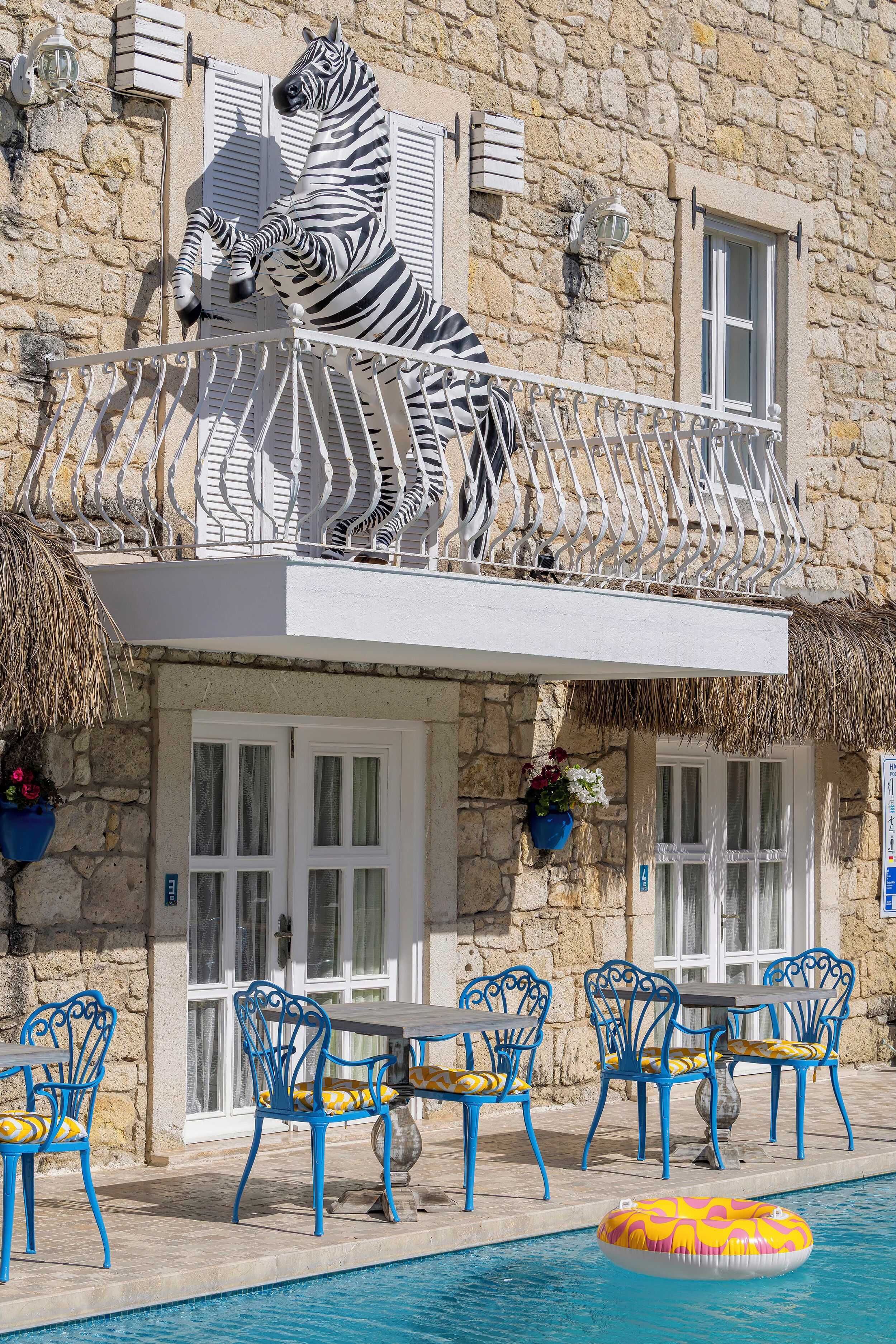 A stone building with a zebra statue on the balcony, outdoor seating, and a pool.