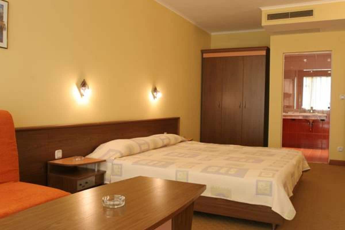 Une chambre d’hôtel avec un lit, une table de chevet en bois, une table et une armoire.