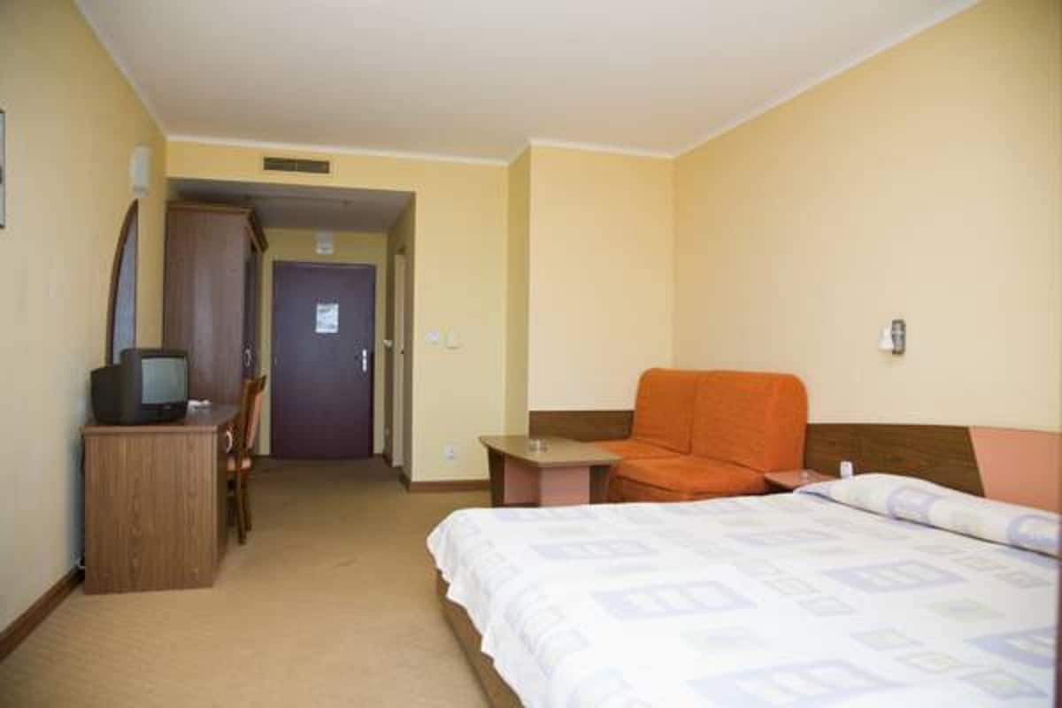 Une chambre d’hôtel avec un lit, un bureau avec une télévision, une chaise orange et une petite table.