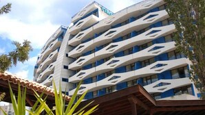 Et moderne hotel med en unik geometrisk facade, flere altaner og et overdækket udendørsområde med planter.