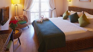 Una habitación de hotel con una cama, un ventilador de techo, una ventana con cortinas, una lámpara, una silla de mimbre y un televisor.
