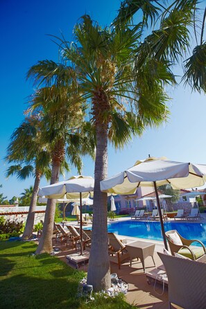 A poolside area with lounge chairs and umbrellas, surrounded by palm trees. - Casaoliva Hotel (Cesme)