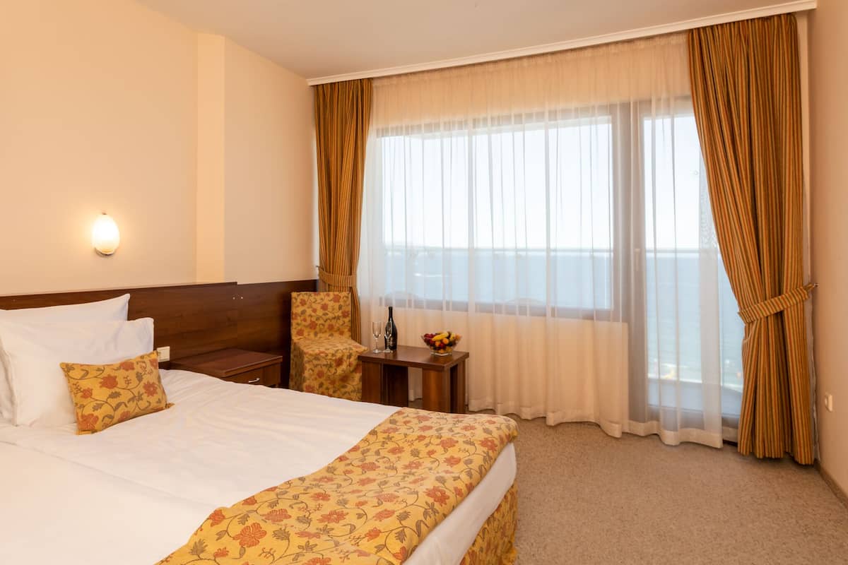 Habitación de hotel con cama, una silla, una mesita con frutero y ventana con cortinas.