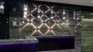 Zona de recepción con diseño moderno, que incluye una pared de mármol, un mostrador de recepción y una barra iluminada en color púrpura.