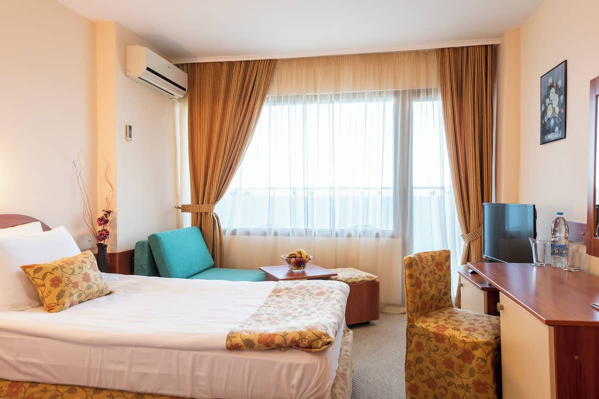 Habitación de hotel con cama, escritorio, silla, televisión y ventana con cortinas.