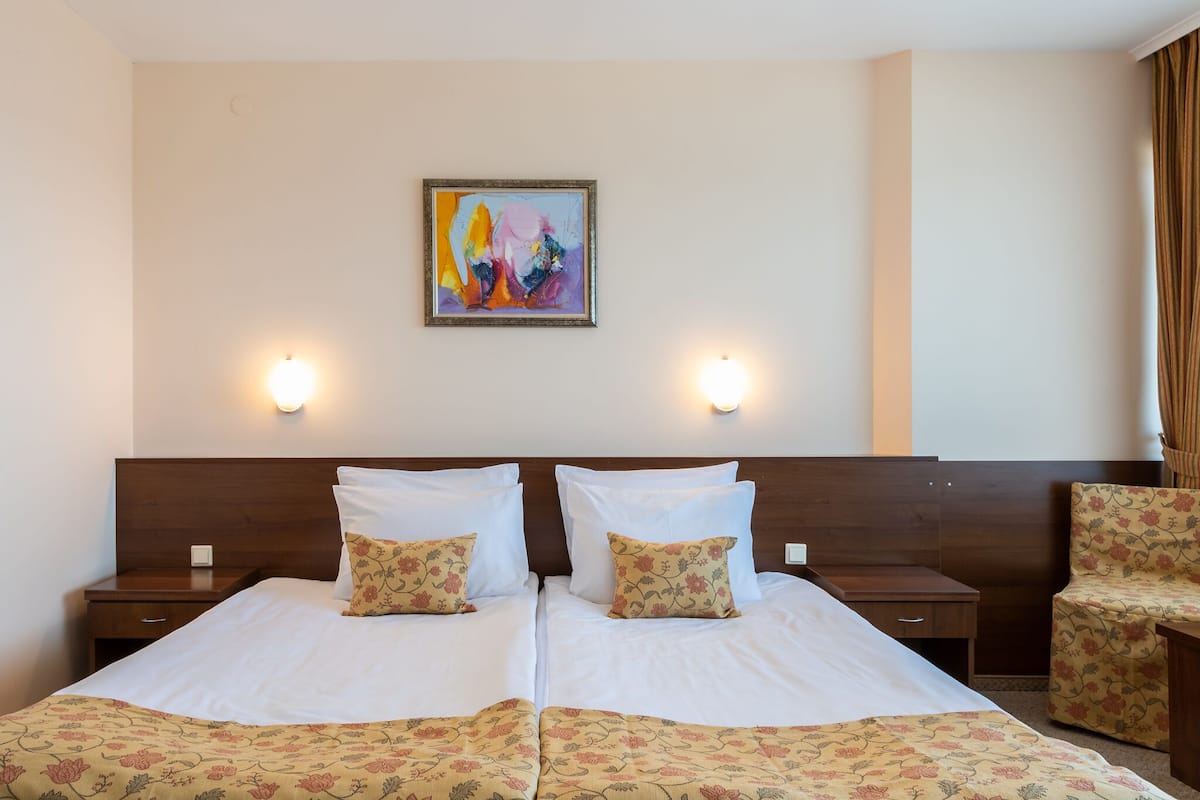Habitación de hotel con dos camas, ropa de cama estampada con motivos florales, un cuadro en la pared y dos lámparas de noche.