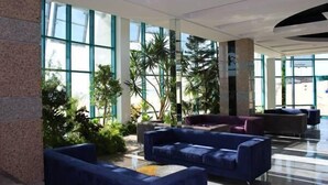 Un vestíbulo amplio con grandes ventanales, un sofá azul y plantas de interior.