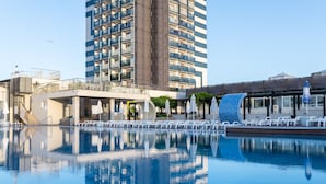 Una piscina con sillas de descanso y sombrillas, rodeada de edificios modernos.