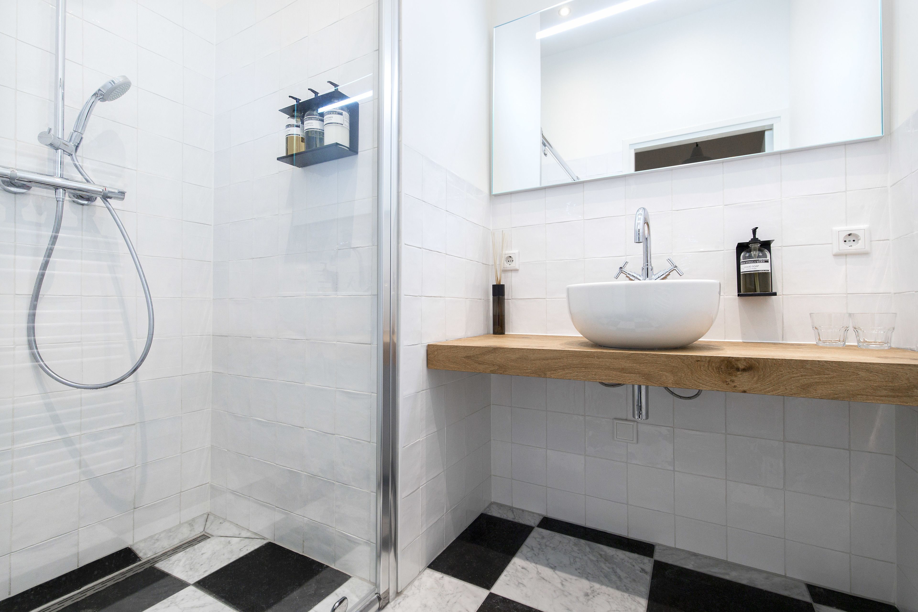 Une salle de bain moderne avec une douche à parois de verre, un lavabo blanc doté d’un plan de toilette en bois et un grand miroir au-dessus du lavabo.