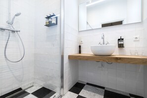 Une salle de bain moderne avec une douche à parois de verre, un lavabo blanc doté d’un plan de toilette en bois et un grand miroir au-dessus du lavabo.