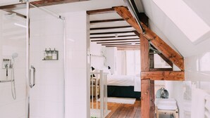 A modern bathroom with a glass shower enclosure, white tiles, and a wooden ceiling beam.