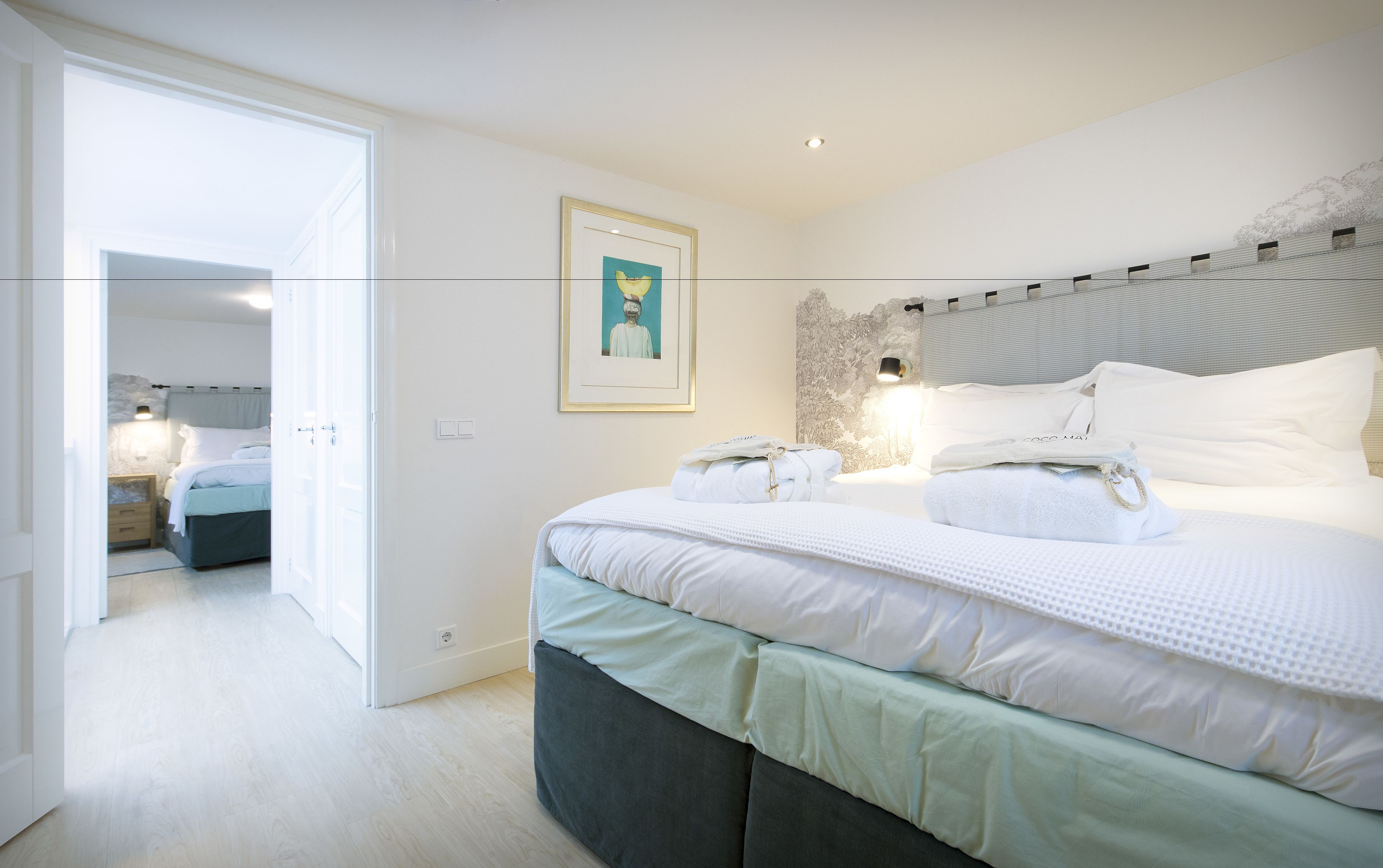 Une chambre moderne avec un grand lit, une table de chevet, une lampe fixée au mur et un tableau encadré.