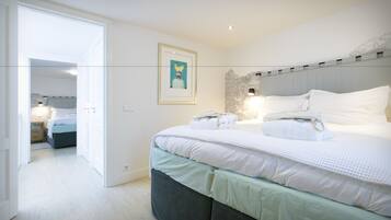 Une chambre moderne avec un grand lit, une table de chevet, une lampe fixée au mur et un tableau encadré.