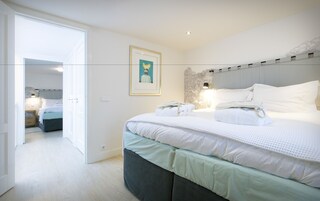 Un dormitorio moderno con una cama grande, una mesita de noche, una lámpara de pared y un cuadro enmarcado.