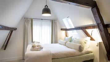 Une chambre avec un plafond en pente, un lit avec des oreillers et une couverture, un luminaire suspendu et une fenêtre avec des rideaux.