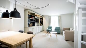 A modern living room with a wooden table, two chairs, a sofa, and a bookshelf.