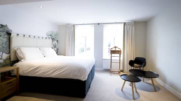 Une chambre moderne avec un grand lit, une table de chevet en bois, une petite table, deux chaises et une fenêtre avec des rideaux.