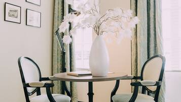 A dining area with a checkered floor, two chairs, a round table, a white vase with flowers, and curtains.