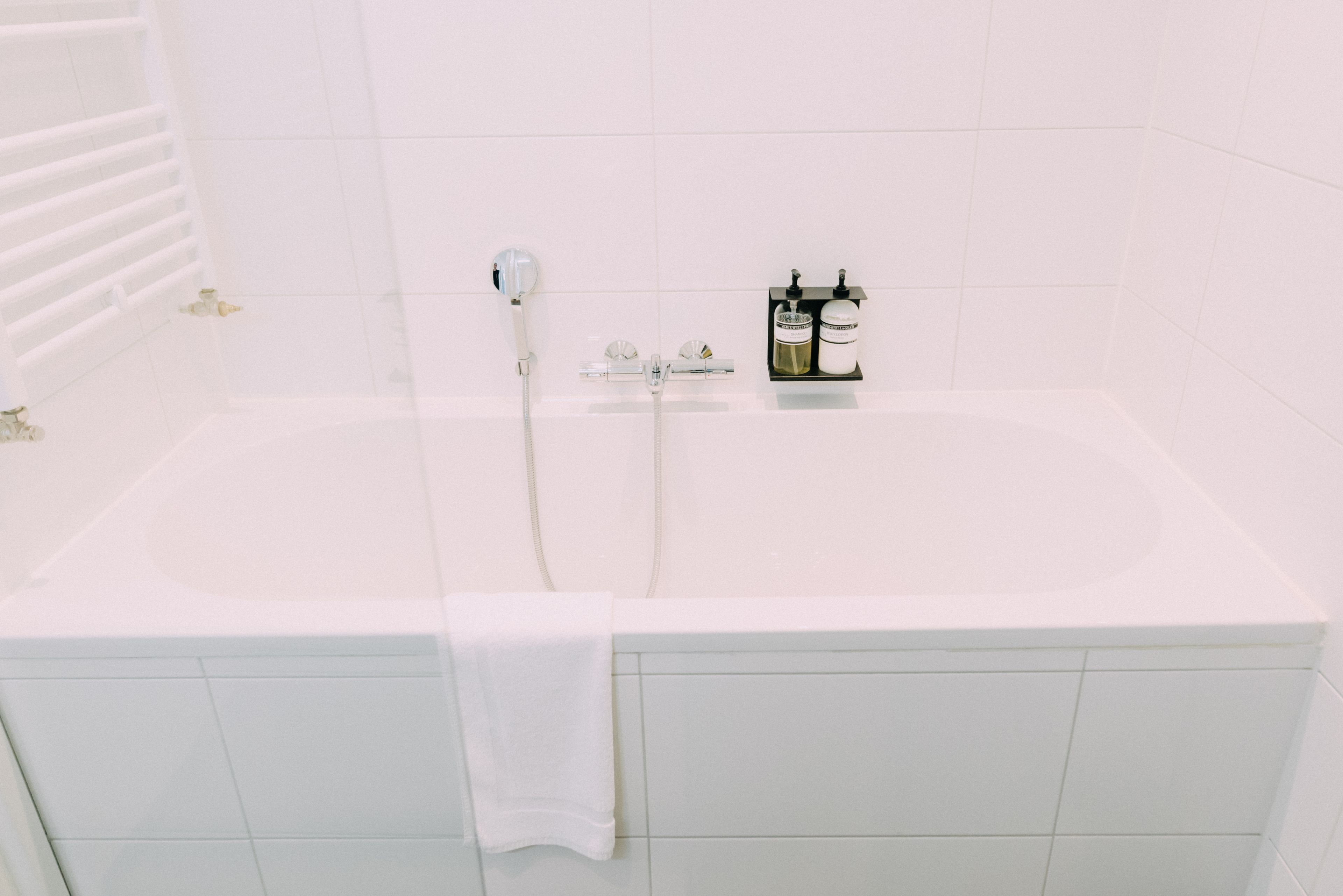A white bathtub with a handheld showerhead, a towel, and two bottles of shampoo on the side.