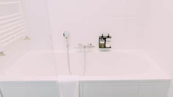 A white bathtub with a handheld showerhead, a towel, and two bottles of shampoo on the side.