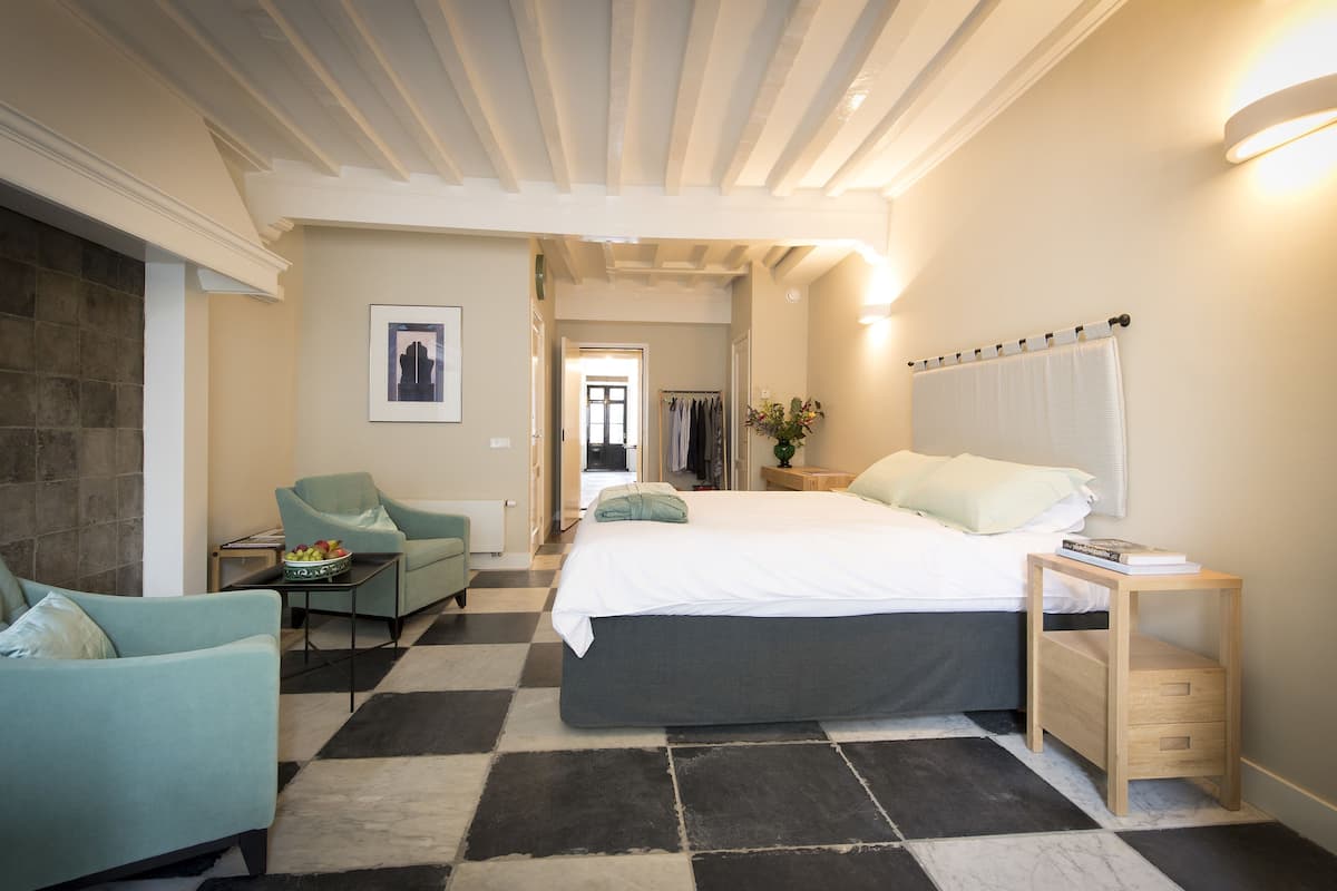 Un dormitorio con cama, una silla, una mesita de noche y una estantería en la pared.