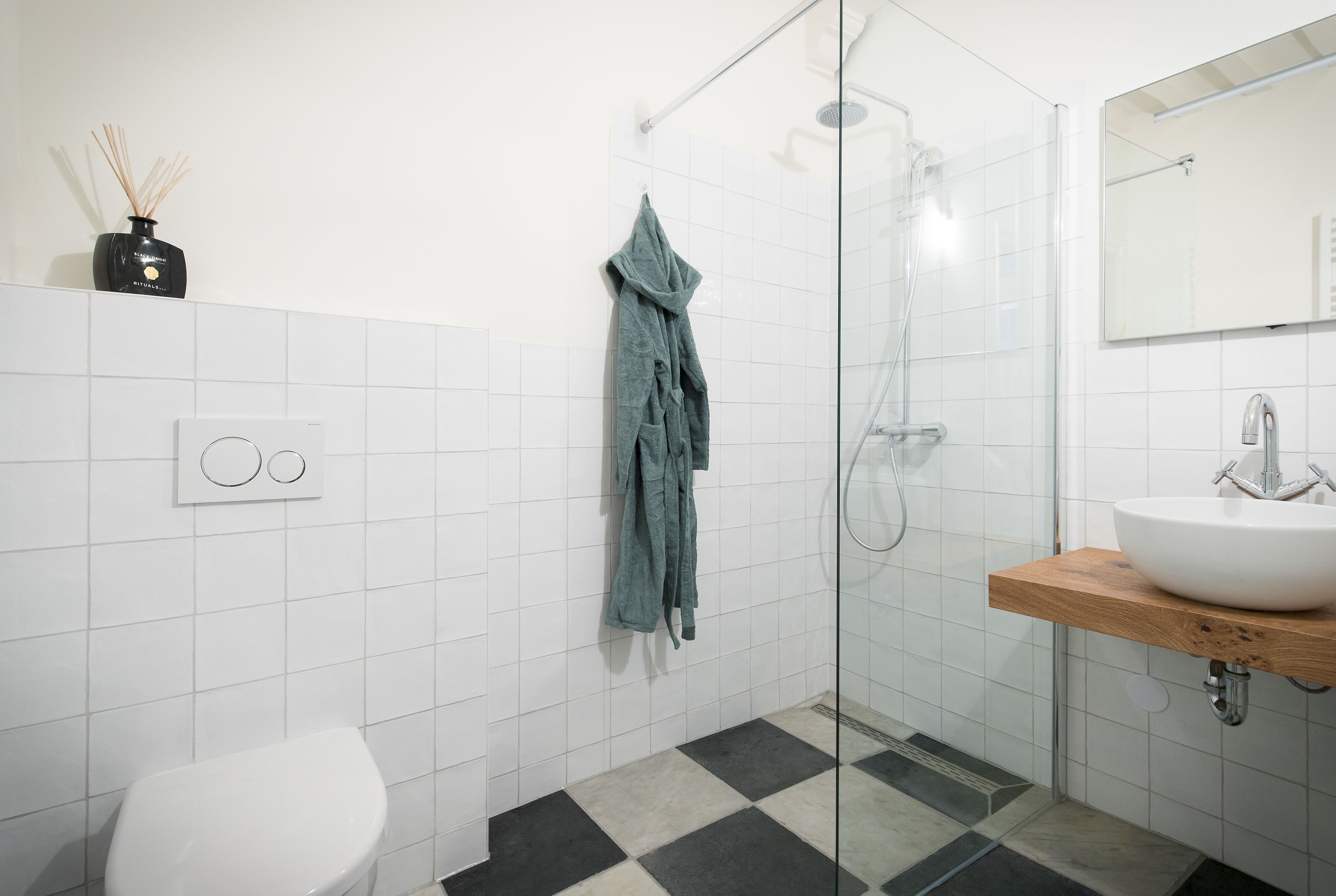A bathroom with a white toilet, a glass-enclosed shower, a wooden vanity with a white sink, and a towel rack with a green towel.
