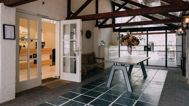 A reception area with a wooden bench, a table with a vase of flowers, and a door leading to a room with a wooden interior.
