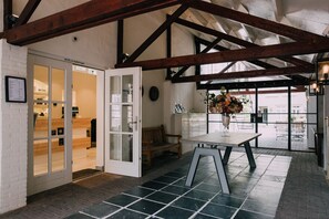 Un espace d’accueil avec un banc en bois, une table ornée d’un vase de fleurs et une porte donnant sur une pièce au décor intérieur en bois.
