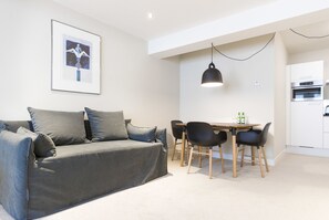 Un salon moderne avec un canapé gris, des chaises noires, une table à manger et un coin cuisine doté de meubles blancs.