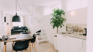 A modern kitchen with white cabinets, a black countertop, and a sink. There is a staircase leading to a loft area.