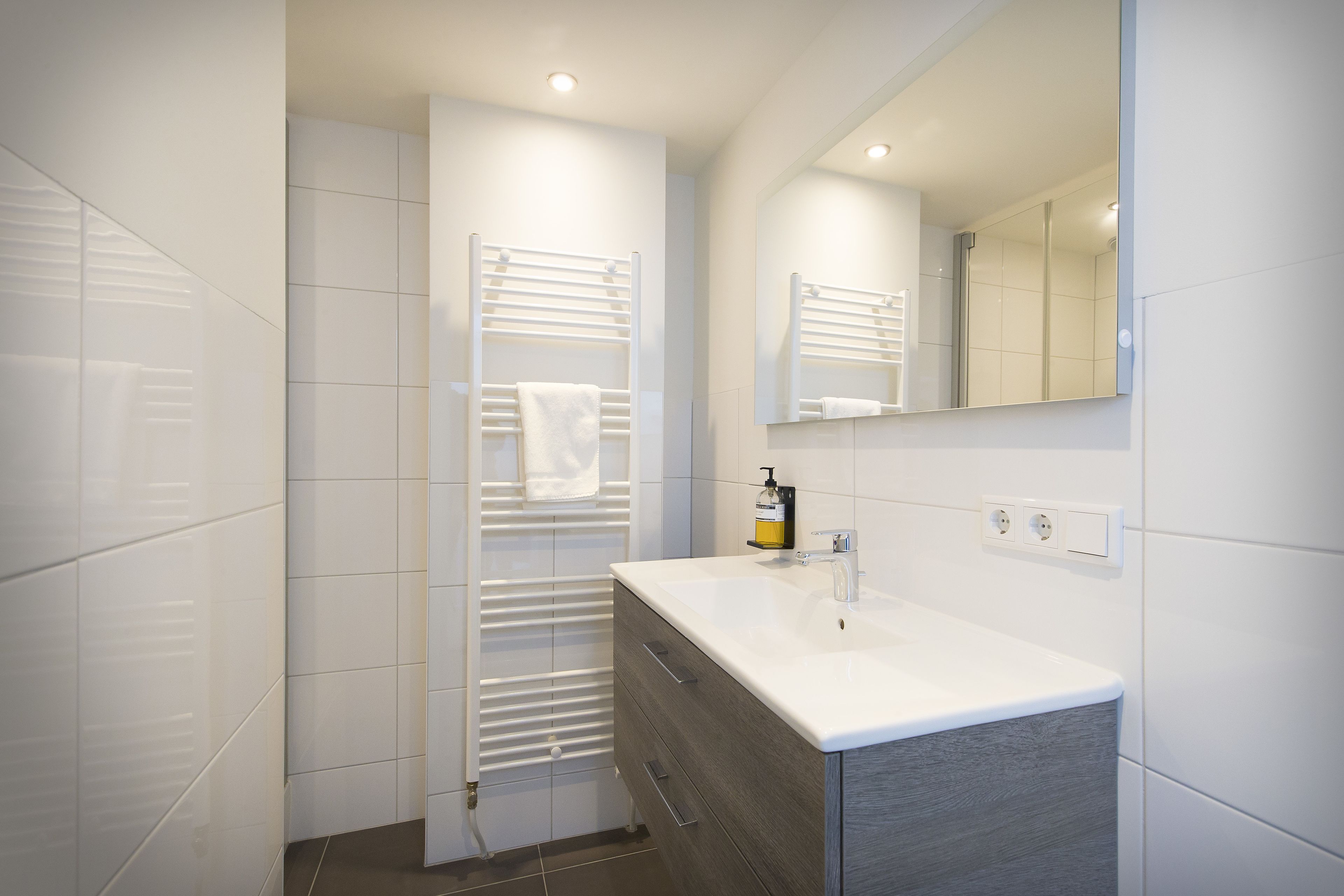 A modern bathroom with a white vanity, a towel rack, and a mirror.