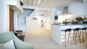 A modern kitchen with a central island, bar stools, and a staircase leading to another level.