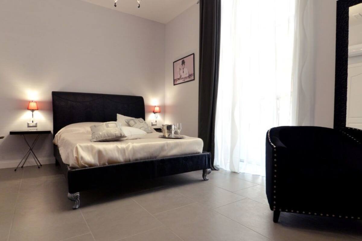A modern bedroom with a black bed, two bedside lamps, a black armchair, and a large mirror.