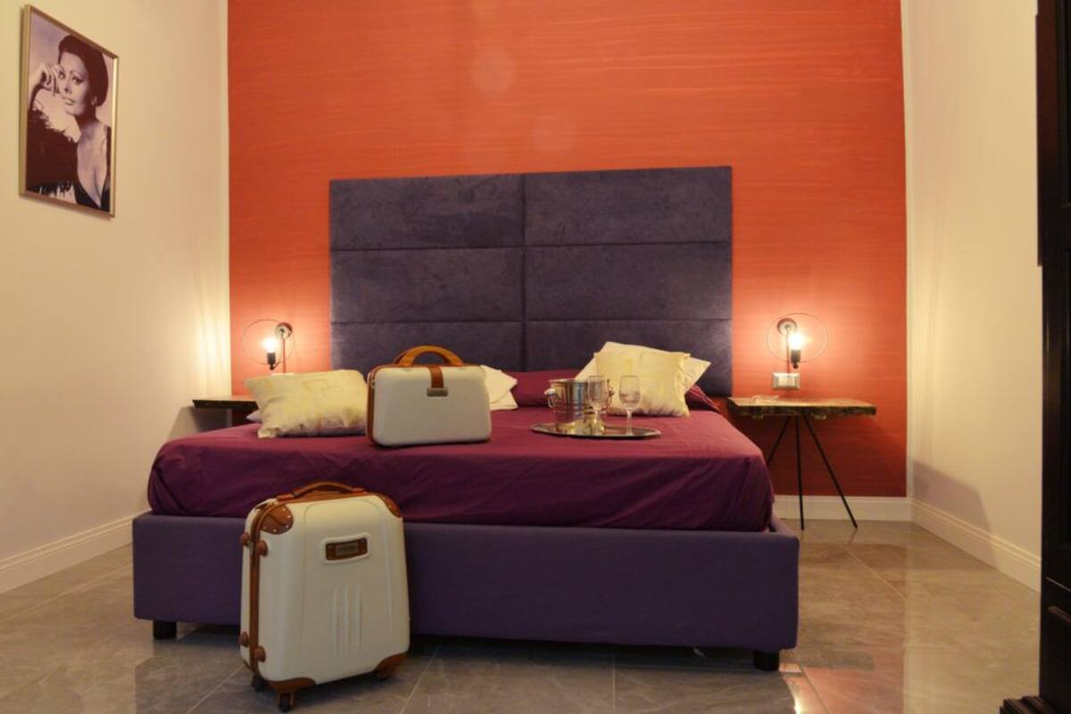 A bedroom with a large bed, two bedside tables, a nightstand, and a suitcase.