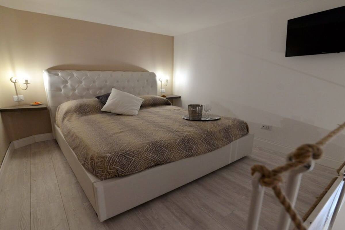 A modern bedroom with a tufted headboard, a large bed, bedside tables with lamps, and a flat-screen TV mounted on the wall.