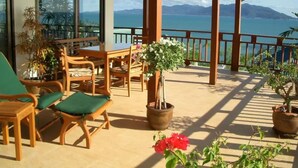 A covered outdoor seating area with wooden furniture and potted plants, overlooking a body of water and mountains. - 4 Bedroom 300 degrees Sea View Villa SDV139A-By Samui Dream Villas (Koh Samui)