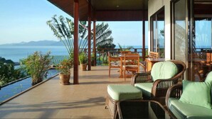 A covered outdoor area with wicker furniture, a table, and chairs, overlooking a body of water and mountains. - 4 Bedroom 300 degrees Sea View Villa SDV139A-By Samui Dream Villas (Koh Samui)