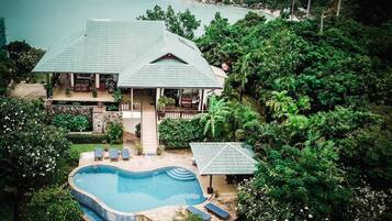 Relax by the spacious outdoor pool surrounded by lush greenery and a serene beach view.
