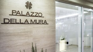 Señalización de 'PALAZZO DELLAMURA', con un interior moderno visible a través de puertas de cristal.