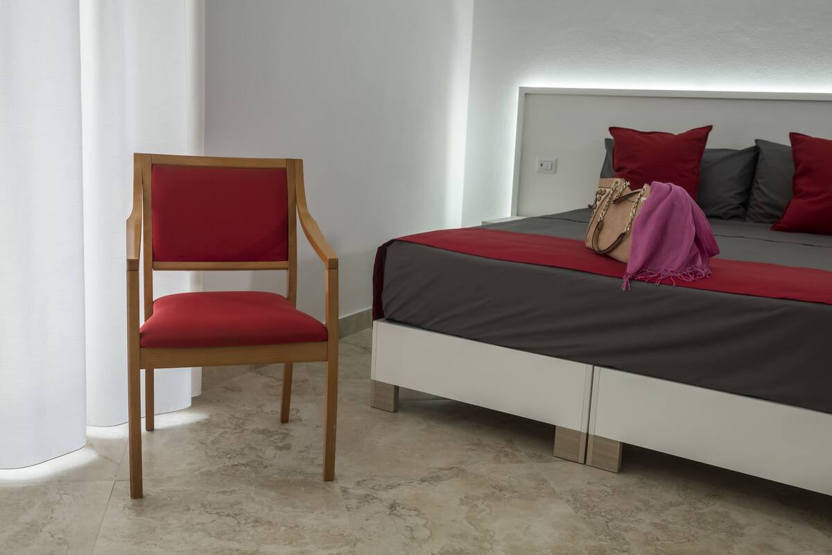 Quarto moderno com uma cama, uma cadeira de madeira e uma mesinha de cabeceira.