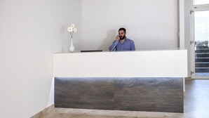 Un mostrador de recepción con un florero, un hombre hablando por teléfono y vistas al exterior a través de un vidrio.