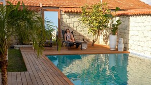 Un espace piscine agrémenté d’un mur en pierre, d’une terrasse en bois et d’une chaise longue.